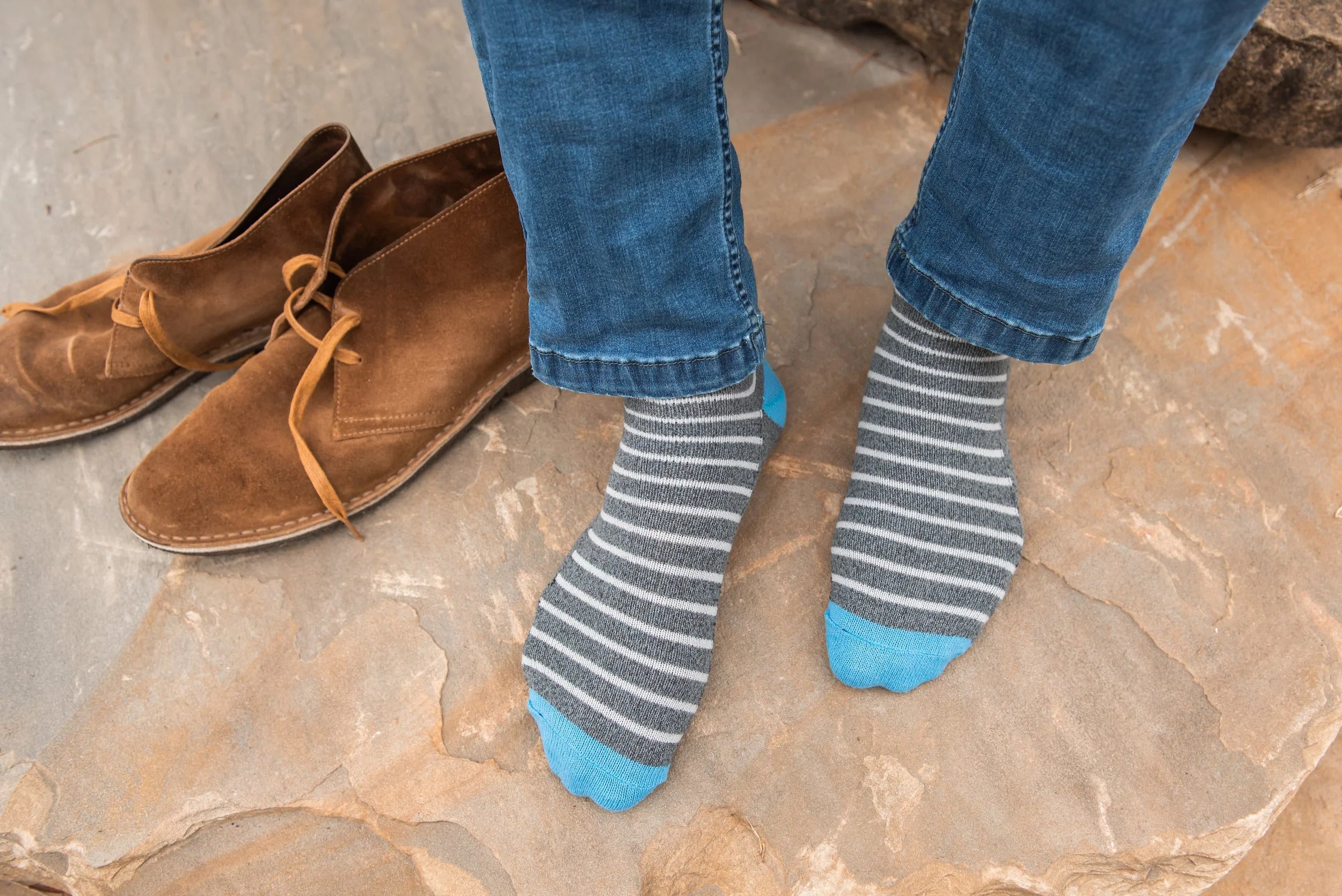 A man's feet wearing grey and white striped socks wit brown boots next to them